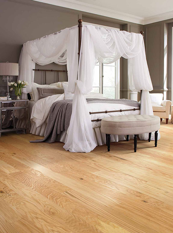 A bedroom with a large four-post canopy bed draped in mosquito netting and an ottoman at the foot of the bed.